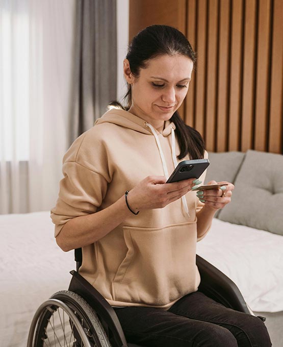 Woman in a wheelchair holding a credit card and her phone.